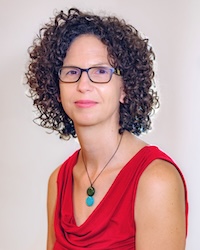 This is a professional portrait of Dr. Peggy Lindner, showing her with dark curly hair, rectangular glasses, and a calm expression. She is wearing a sleeveless red blouse and a necklace with green and turquoise pendants, set against a plain light background.